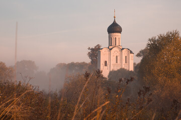 Old Russian Orthodox church lit by the rising sun above autumn forest in a light mist