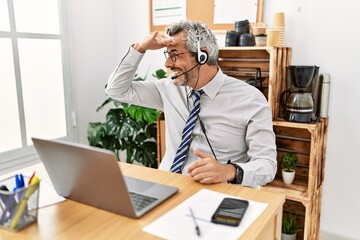 Middle age hispanic business man working at the office wearing operator headset very happy and smiling looking far away with hand over head. searching concept.