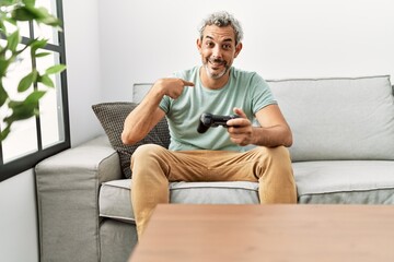 Middle age hispanic man playing video game sitting on the sofa pointing finger to one self smiling happy and proud