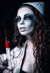 Horror shot: scary wicked mad nurse (doctor) with bloody syringe in hand. Zombie woman (living dead)