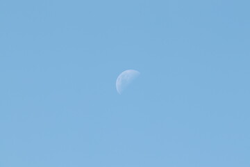 A moon in daylight blue skies