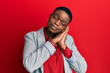 Young african american woman wearing business jacket and glasses sleeping tired dreaming and posing with hands together while smiling with closed eyes.