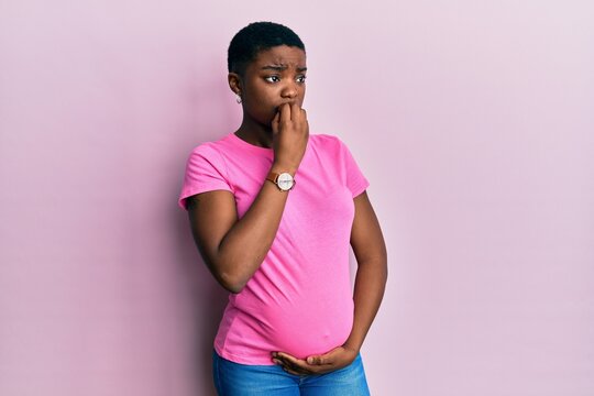 Young african american woman expecting a baby, touching pregnant belly looking stressed and nervous with hands on mouth biting nails. anxiety problem.