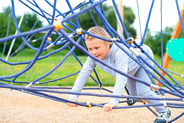 Little girl climbing in an adventure park. The girl loves to climb in the adventure of the rope course. Little girl on the rope obstacle course - obrazy, fototapety, plakaty