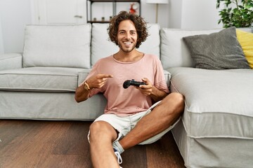 Young hispanic man playing video game holding controller at home smiling happy pointing with hand and finger © Krakenimages.com