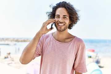 Young hispanic man smiling happy talking on the smartphone at the beach.