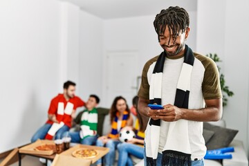 Group of young friends watching and supporting soccer match at home. Man smiling happy and using smartphone.