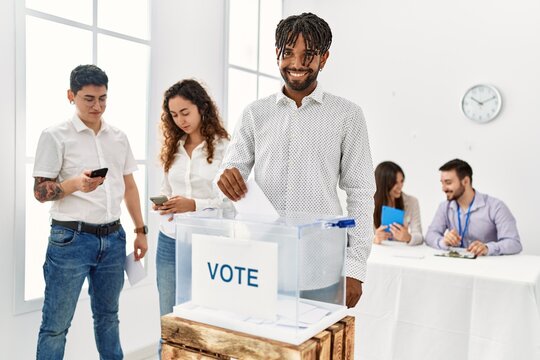 Young voter man smiling happy putting vote in voting box at electoral center.