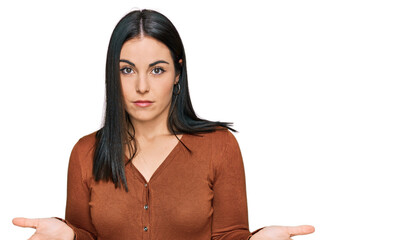 Young hispanic woman wearing casual clothes clueless and confused expression with arms and hands...