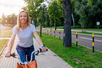 Obraz premium A pretty young woman in a white t-shirt is riding a city bike. Clean, sustainable city transport.