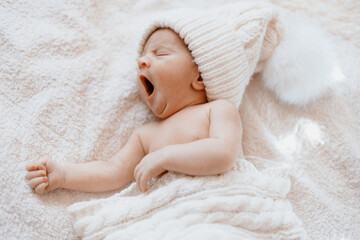 cute yawning newborn baby in a white knitted hat .