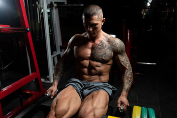 Fototapeta na wymiar Muscular Man Exercising Quadriceps On Machine
