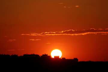 Fototapeta premium Sunset over city, scenic view. Setting sun and orange sky with dark dramatic clouds above black silhouettes of residential buildings