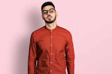 Young hispanic man with beard wearing business shirt and glasses relaxed with serious expression on...