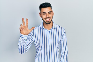 Young hispanic man with beard wearing casual striped shirt showing and pointing up with fingers number three while smiling confident and happy.