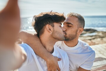 Young gay couple kissing making selfie by the camera at the beach.