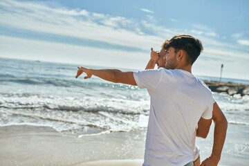 Young gay couple on back view looking to the horizon at the beach.