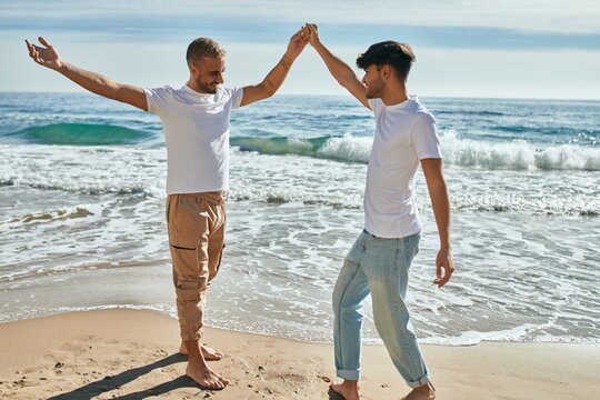 Young gay couple smiling happy dancing at the beach.