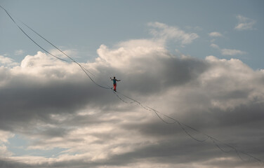 A tightrope walker walks along a long, high-stretched rope. Dramatic sky in background