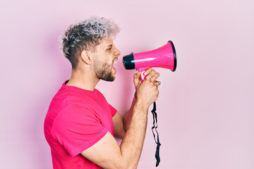 Young hispanic man screaming with megaphone over pink background