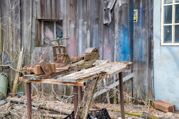 An old workbench with tools including a vice sits decaying outside an abandoned workshop in the...