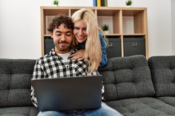 Young couple using laptop sitting on the sofa at home.