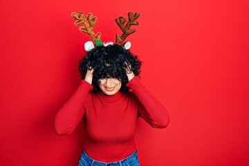 Young middle east woman wearing cute christmas reindeer horns suffering from headache desperate and stressed because pain and migraine. hands on head.