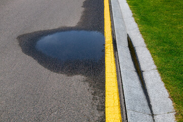 puddle on asphalt road with stormwater on the road side with a ditch for water after rain and a...