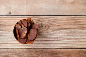 Homemade jerked dried meat or biltong with spices on a wooden background. Beer snack concept. Selective focus, copyspace.
