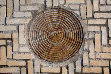 iron rusty round manhole on the sidewalk paved with stone tiles top view, old sewer hatch on a...