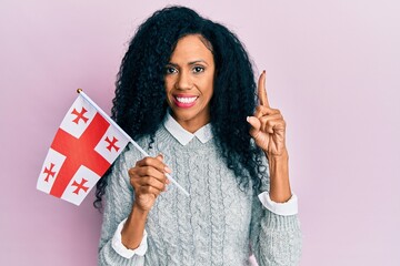 Middle age african american woman holding georgia flag smiling with an idea or question pointing finger with happy face, number one