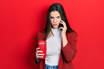 Young brunette teenager talking on smartphone and drinking coffee skeptic and nervous, frowning upset because of problem. negative person.