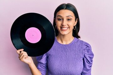 Young hispanic woman holding vinyl disc looking positive and happy standing and smiling with a confident smile showing teeth