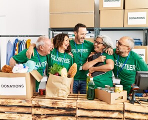 Group of middle age volunteers smiling happy and hugging standing at charity center.