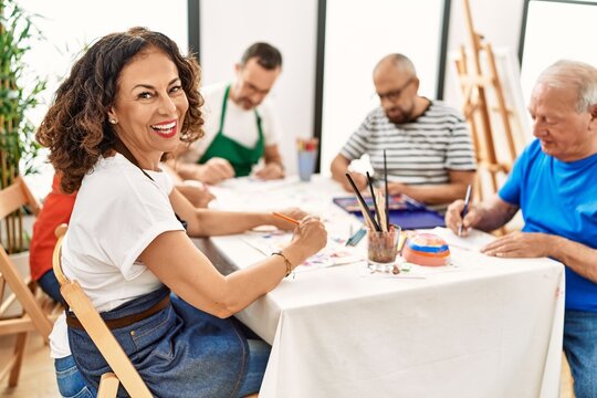 Group of middle age draw students sitting on the table drawing at art studio. Woman smiling happy looking to the camera.