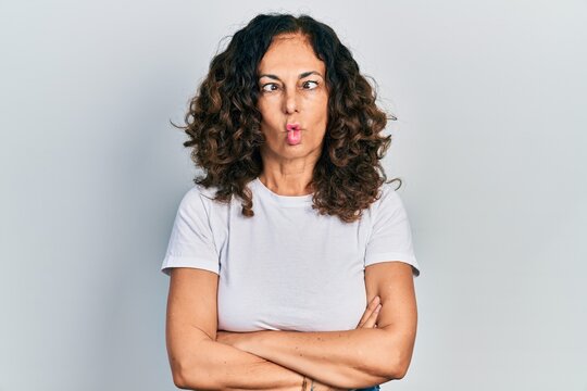 Middle age hispanic woman with arms crossed gesture making fish face with mouth and squinting eyes, crazy and comical.