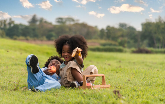 Happy family African kids boy and girl eat apple and banana sit picnic on meadow.