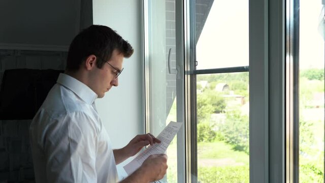 man examines papers while standing by the window