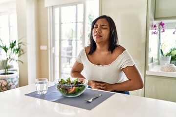 Obraz na płótnie Canvas Young hispanic woman eating healthy salad at home with hand on stomach because indigestion, painful illness feeling unwell. ache concept.