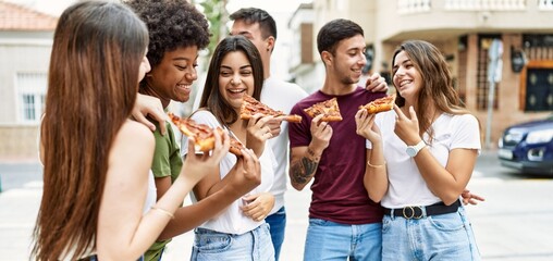 Group of young friends smiling happy eating pizza standing at the city.