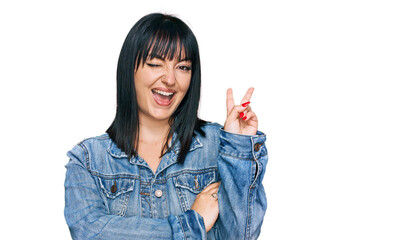 Young hispanic woman wearing casual clothes smiling with happy face winking at the camera doing victory sign. number two.