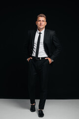 A handsome young man in a stylish black suit poses on a black background. A stylish business man. A big businessman.