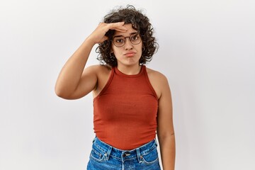 Young hispanic woman wearing glasses standing over isolated background worried and stressed about a problem with hand on forehead, nervous and anxious for crisis