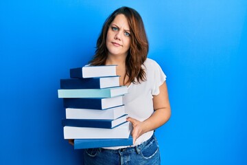 Young caucasian woman holding a pile of books clueless and confused expression. doubt concept.
