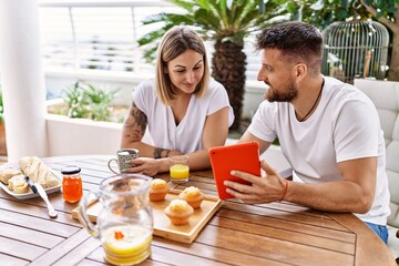 Young couple having breakfast using touchpad at terrace.