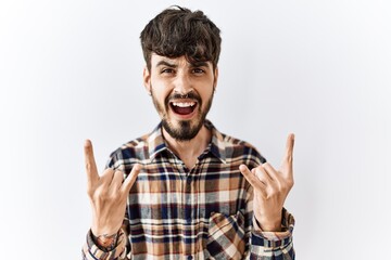 Hispanic man with beard standing over isolated background shouting with crazy expression doing rock symbol with hands up. music star. heavy concept.