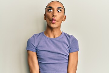 Hispanic man wearing make up and long hair wearing casual t shirt making fish face with lips, crazy and comical gesture. funny expression.