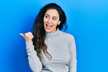 Fototapeta premium Young hispanic woman wearing casual clothes smiling with happy face looking and pointing to the side with thumb up.