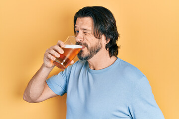 Middle age caucasian man with beard drinking a pint glass of fresh beer