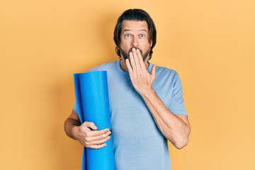Middle age caucasian man holding yoga mat covering mouth with hand, shocked and afraid for mistake....